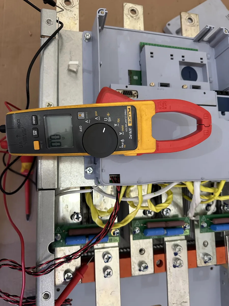 Alicate amperímetro e pontas de prova sobre um soft starter aberto, em bancada.